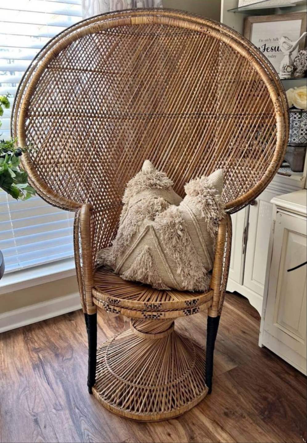 Rattan peacock chair with beige tasseled pillows in a home interior featuring dark wood floors