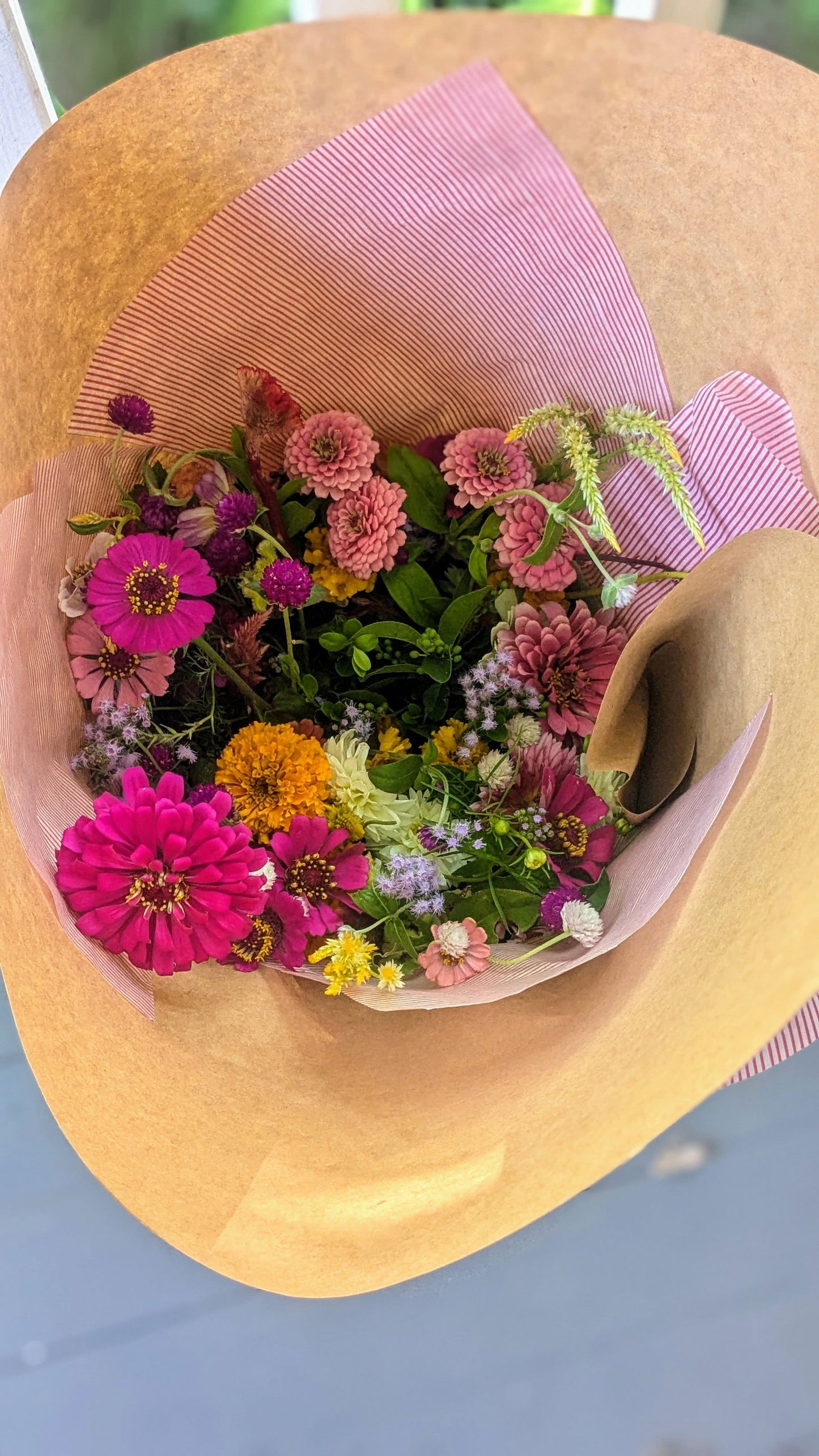 Kraft paper bouquet featuring vibrant zinnias, globe amaranth, and yellow marigolds in a pink striped wrapper
