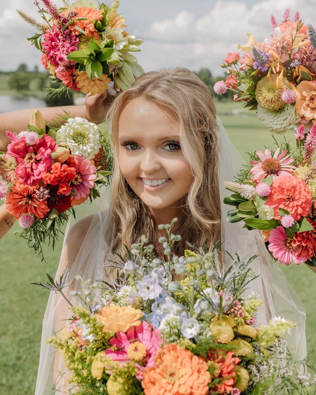 Photography a bride outdoors holding vibrant bouquets featuring zinnias dahlias and delphiniums against a verdant landscape