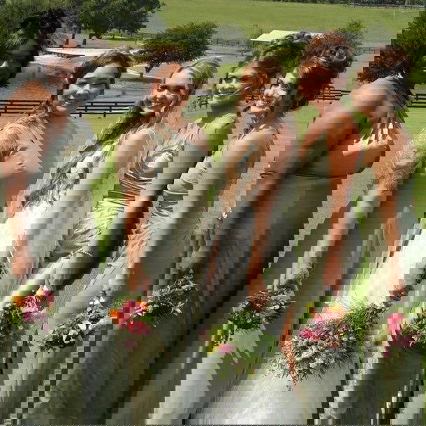 A group in light dresses holds colorful bouquets from Blessings Grow Meadows’ DIY Event Flowers + Fresh Cut Greenery Bloom Buckets (Metter, GA Pick-Up), standing outdoors on a sunny day amid fields and trees; the image has heavy diagonal glitches.