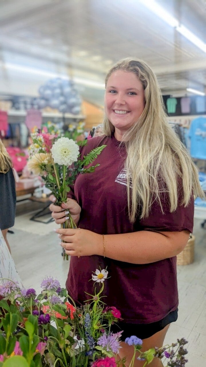 Photograph young woman holding a bouquet of wildflowers including a white dahlia and a unique spiky flower in a shop with blurred background
