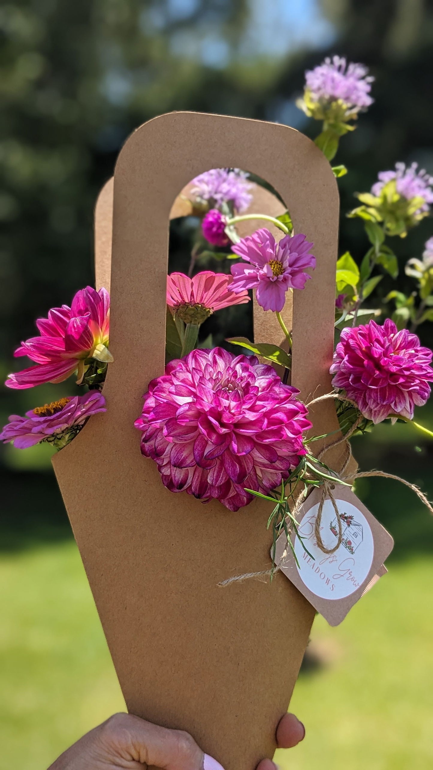 Kraft paper flower arrangement by Blossoms of Meadows featuring dahlias, zinnias, and globe amaranth in vibrant pinks and purples outdoors
