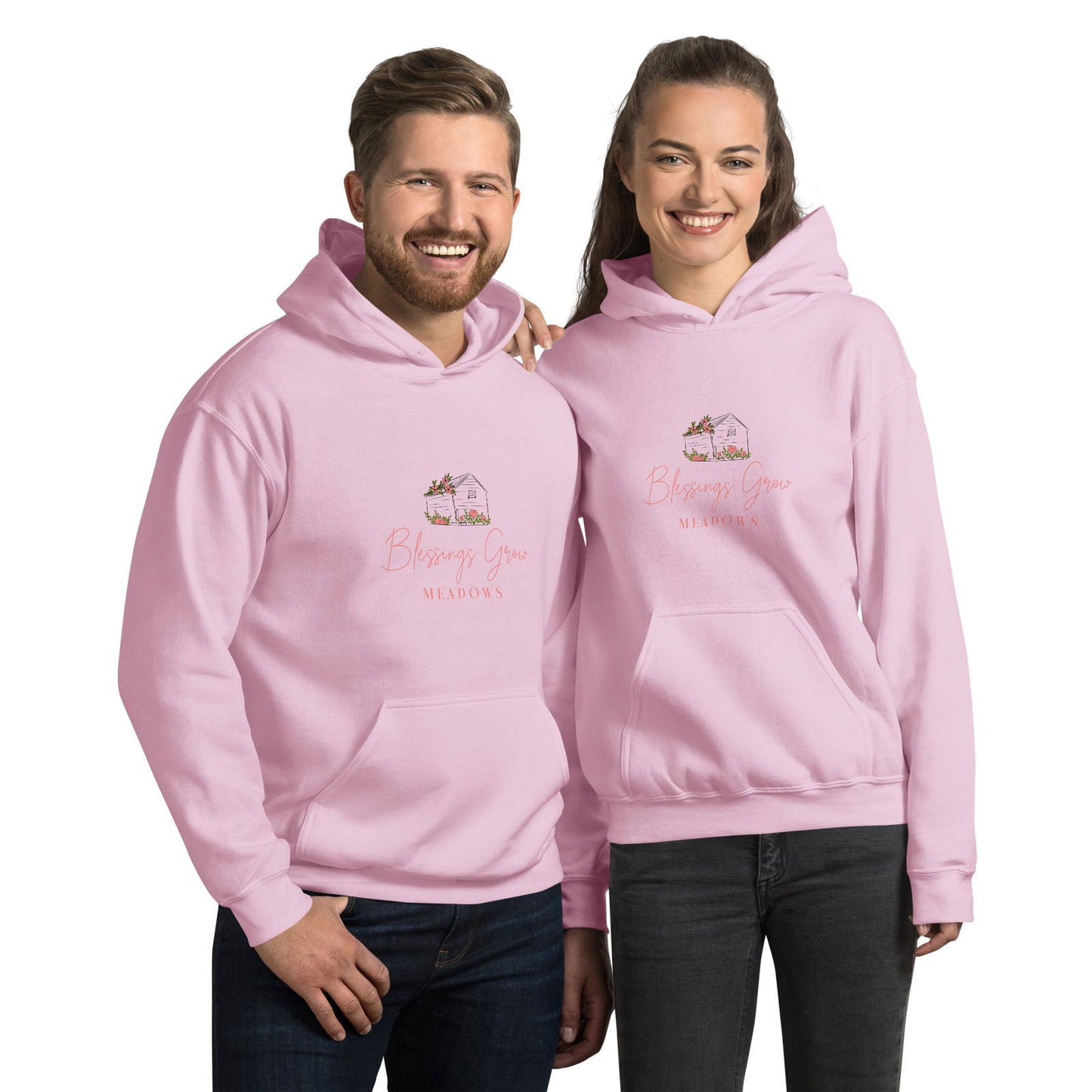 Apparel graphic design featuring a pale pink Blessings Grow Meadows hoodie with a charming cottage illustration adorned with peach-colored flowers and script lettering on a couple.
