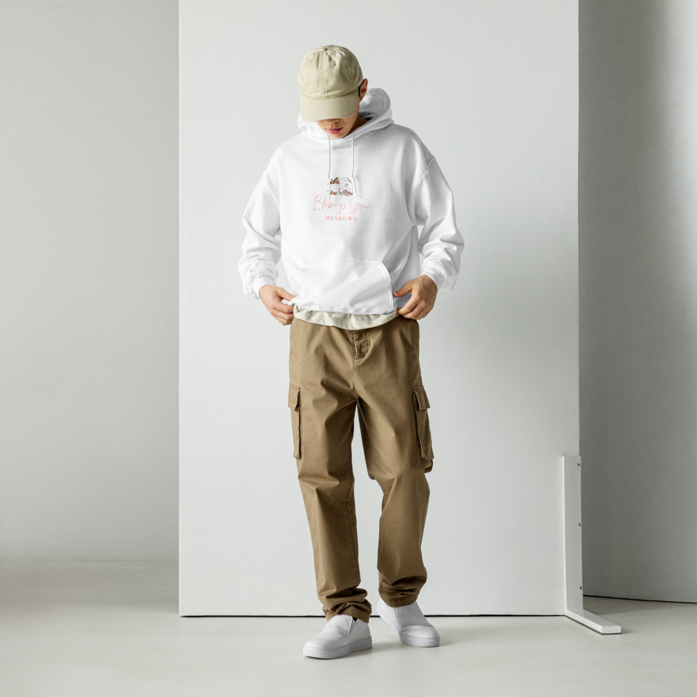Model wearing a white Happiness Farm Meadows hoodie featuring a whimsical illustration of a greenhouse, pink script lettering, and beige cargo pants against a minimalist white backdrop.
