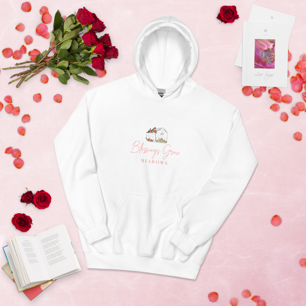 White Blessings Grow Meadows hoodie featuring a floral farmhouse illustration against a pink background with red roses and rose petals a book and notecards