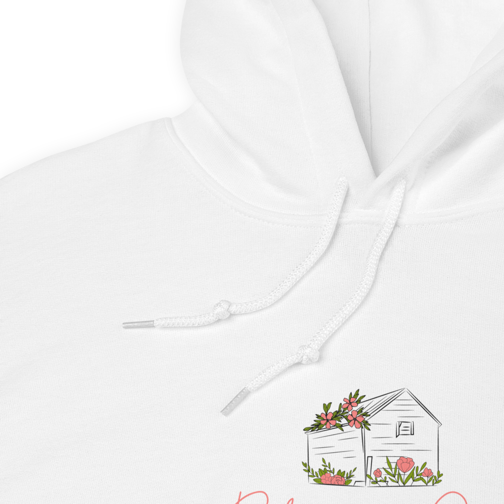White hoodie featuring a line drawing of a floral adorned house with pink flowers and greenery suggesting a cozy cottage setting