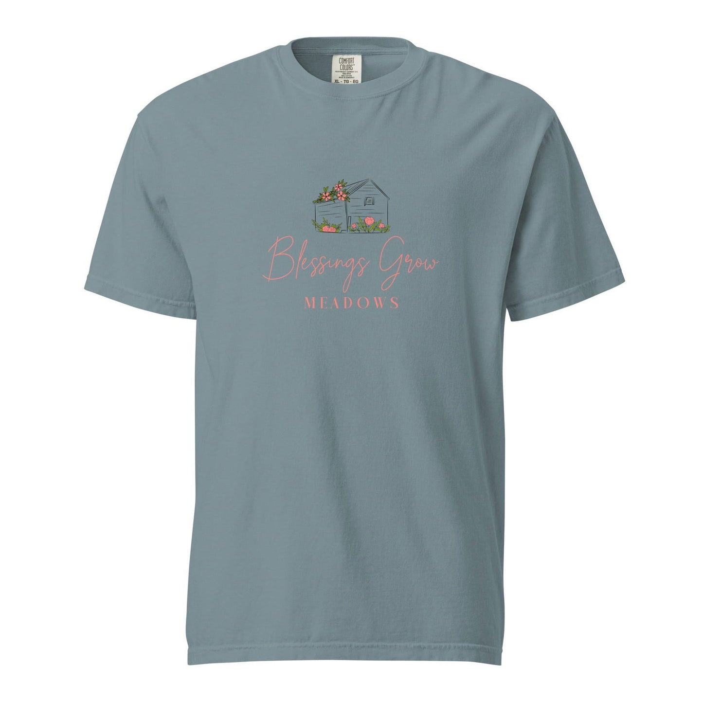 Comfort Colors t-shirt featuring a drawing of a house with pink flowers in a meadow with the text Blessings Grow Meadows in coral script