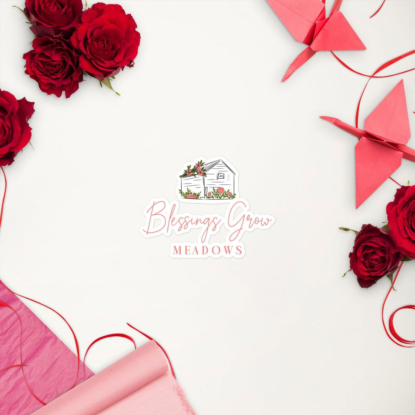 Graphic design featuring a hand-drawn house illustration surrounded by red roses and origami cranes on a white background showcasing Blessings Grow Meadows logo with pink text and floral accents