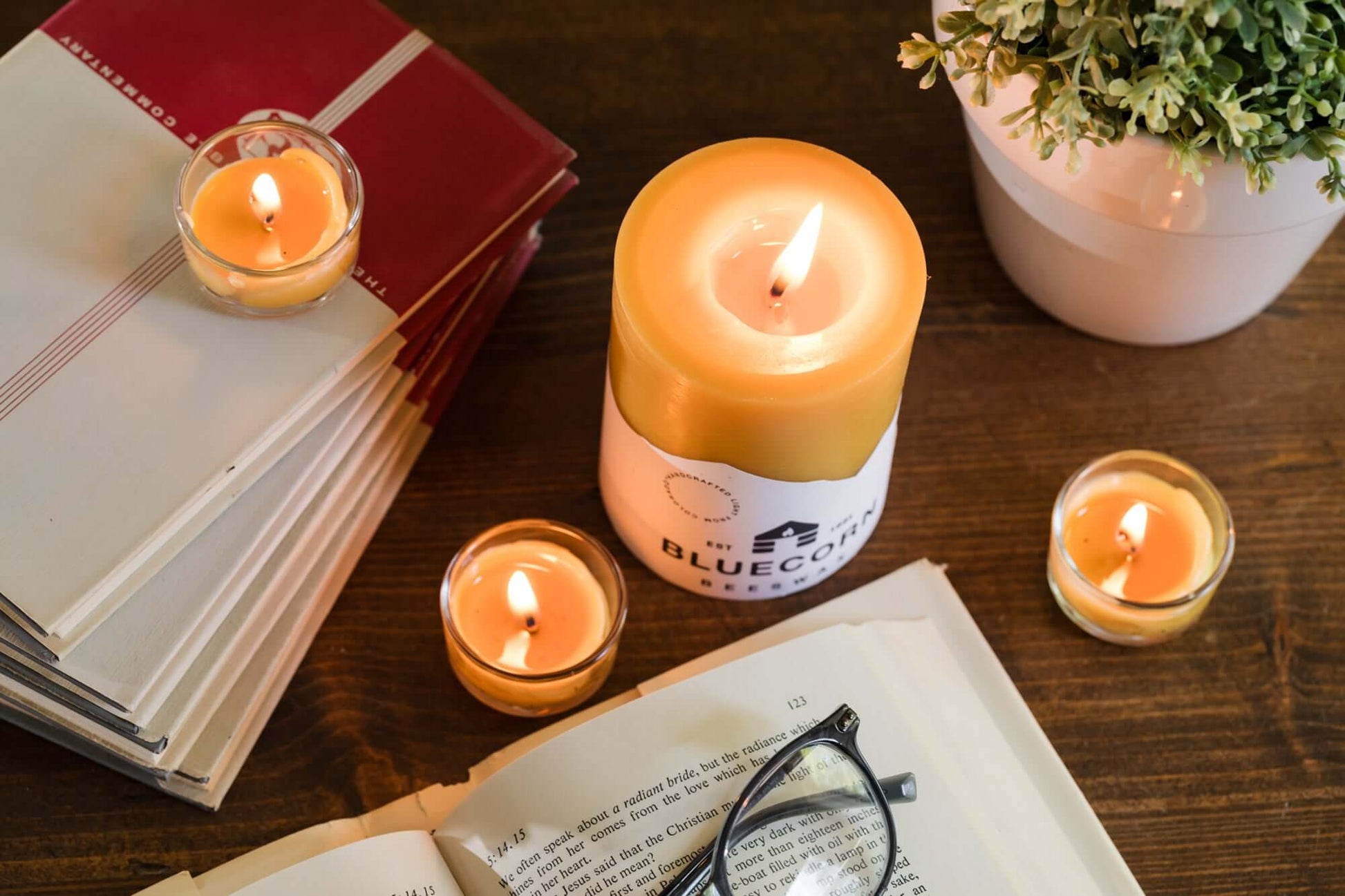 Bluecorn Candles pure beeswax pillar candles with labels, placed near books, glasses, and tea lights in glass holders.
