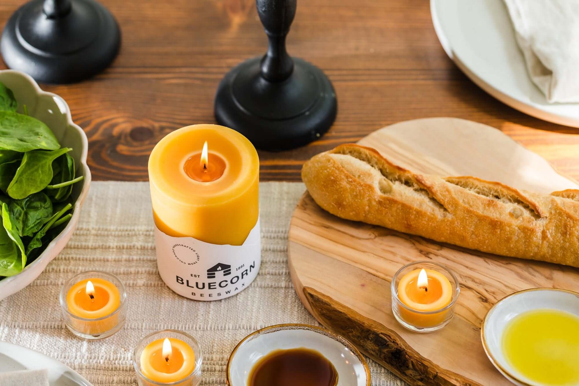 Bluecorn Candles pure beeswax pillar candle and tea lights in glass holders on summer dining table with loaf of bread.