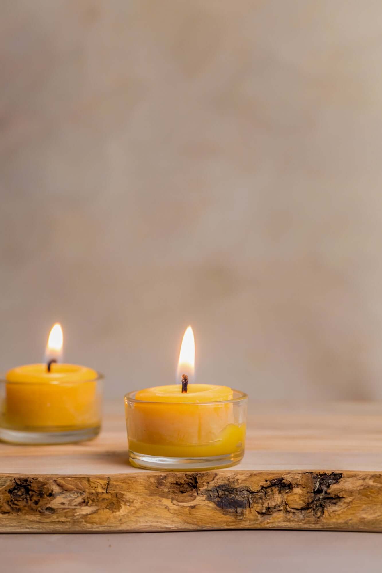 Bluecorn Candles pure beeswax tea light candles in refillable glass holders on a wooden slab, showing warm, natural candlelight.