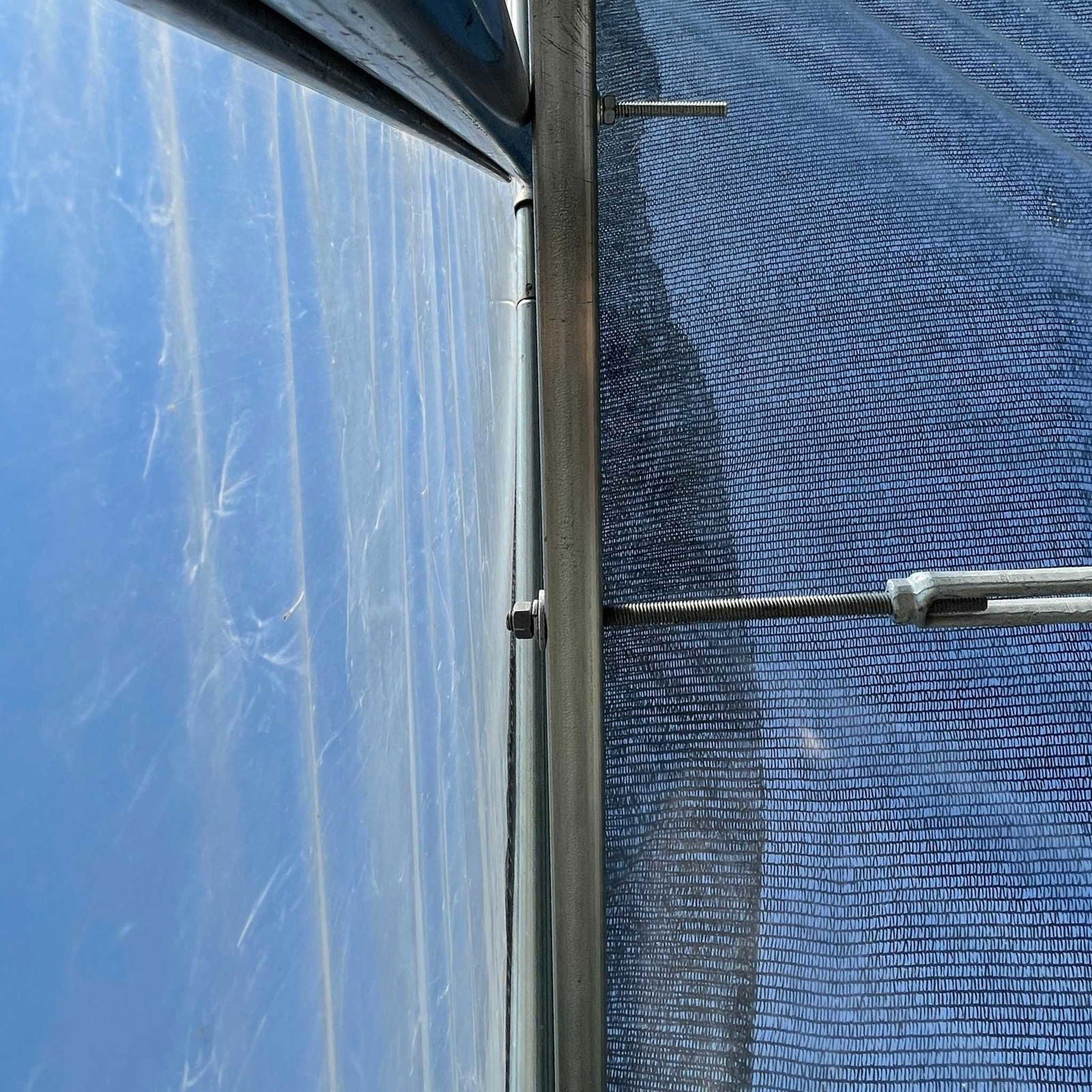 Close-up of Bootstrap Farmer’s Horizontal Bar Kit, showing bolts and tension rods supporting translucent material, possibly on a hoop house, against a bright blue sky. The angled shot highlights the kit’s lines and textures.