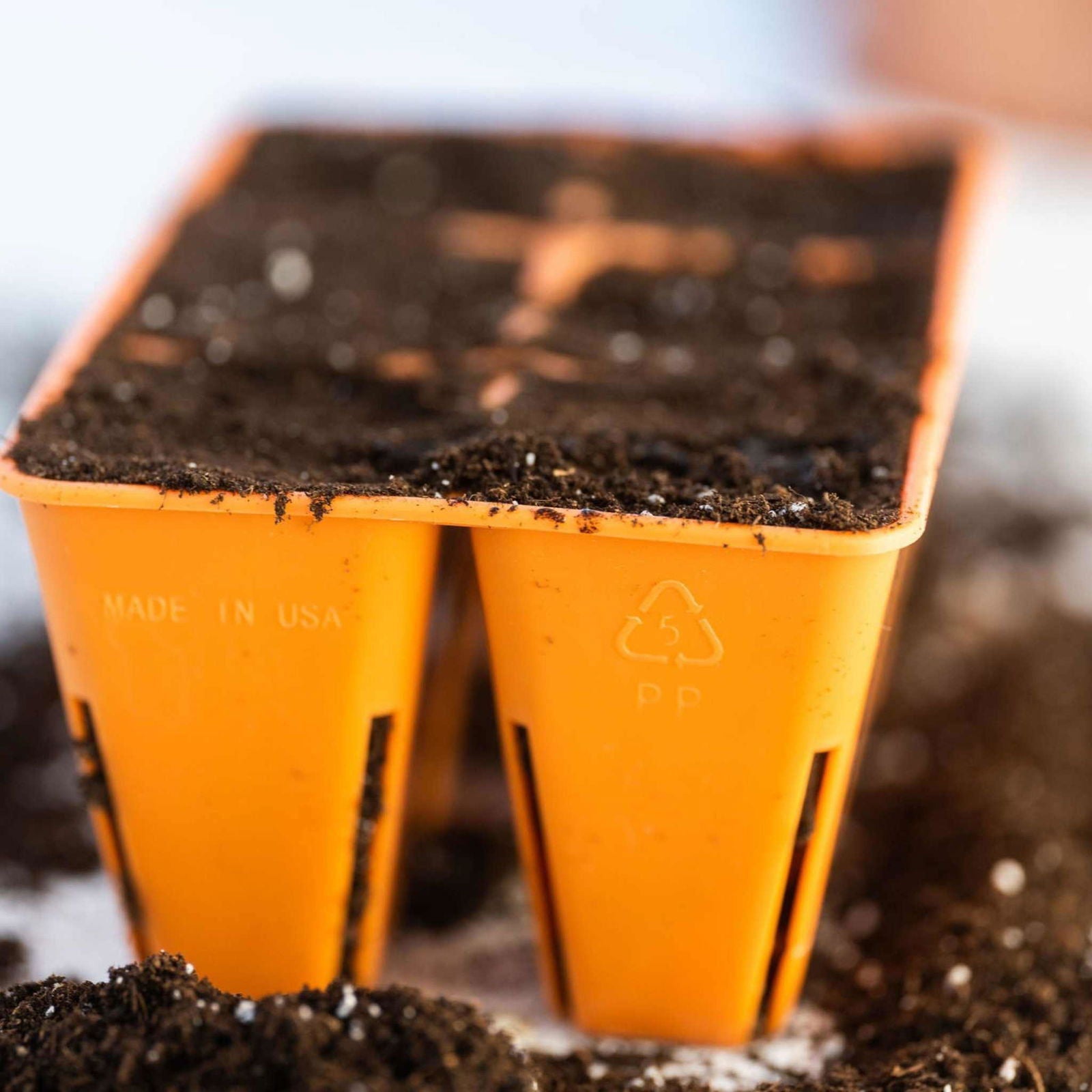 Close-up of two Bootstrap Farmer 6 Cell Plug Tray Inserts Colors, orange in color and filled with soil. The trays are labeled Made in USA and display the recycling symbol 5 PP.