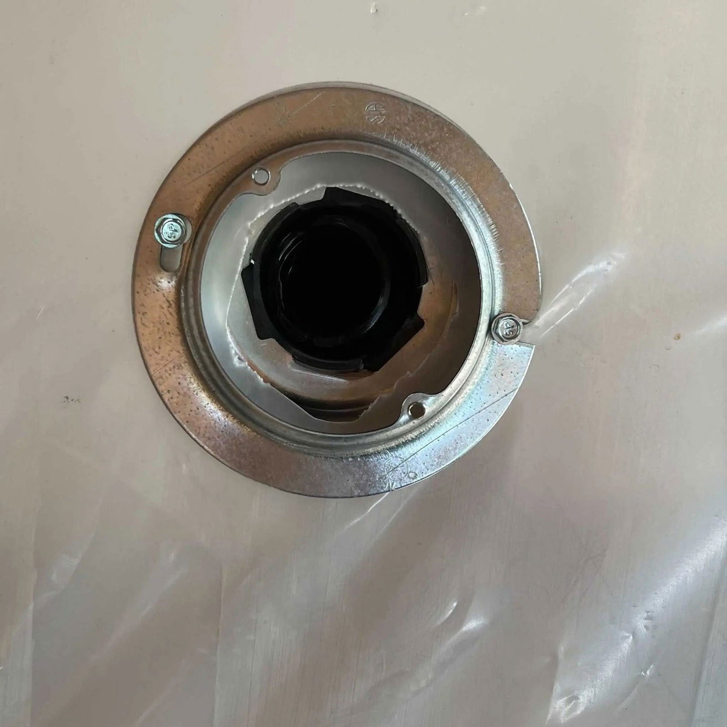 A close-up of the Bootstrap Farmer Greenhouse Air Inflation Kit shows a round metal flange with two screws, mounted on a surface, and a black pipe in the center partially covered by clear greenhouse plastic to help reduce condensation.