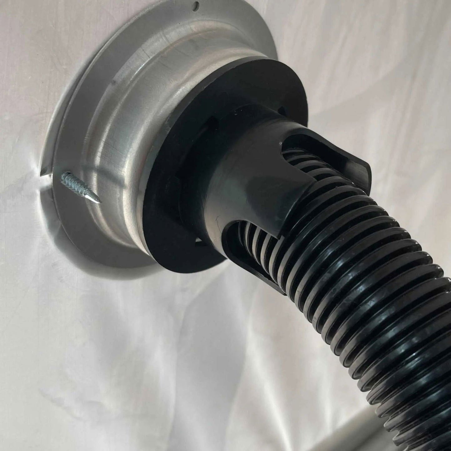 Close-up of a black ribbed hose connected to a metal fitting on a white surface with a visible screw—part of the Bootstrap Farmer Greenhouse Air Inflation Kit, designed to reduce condensation.