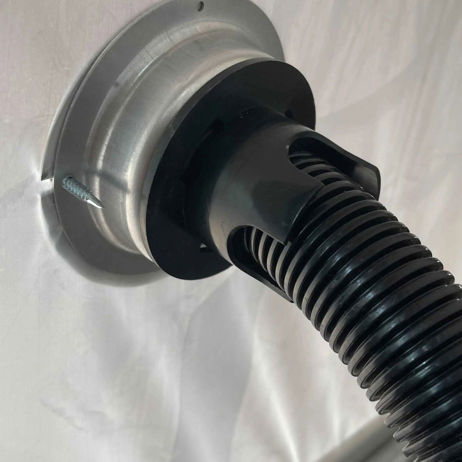Close-up of a black ribbed hose connected to a metal fitting on a white surface with a visible screw—part of the Bootstrap Farmer Greenhouse Air Inflation Kit, designed to reduce condensation.