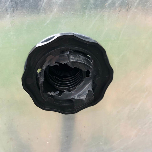 A close-up of a black plastic threaded opening with jagged, torn edges on a surface, possibly part of a damaged Bootstrap Farmer Air Inflation Jumper Hose used in greenhouses.