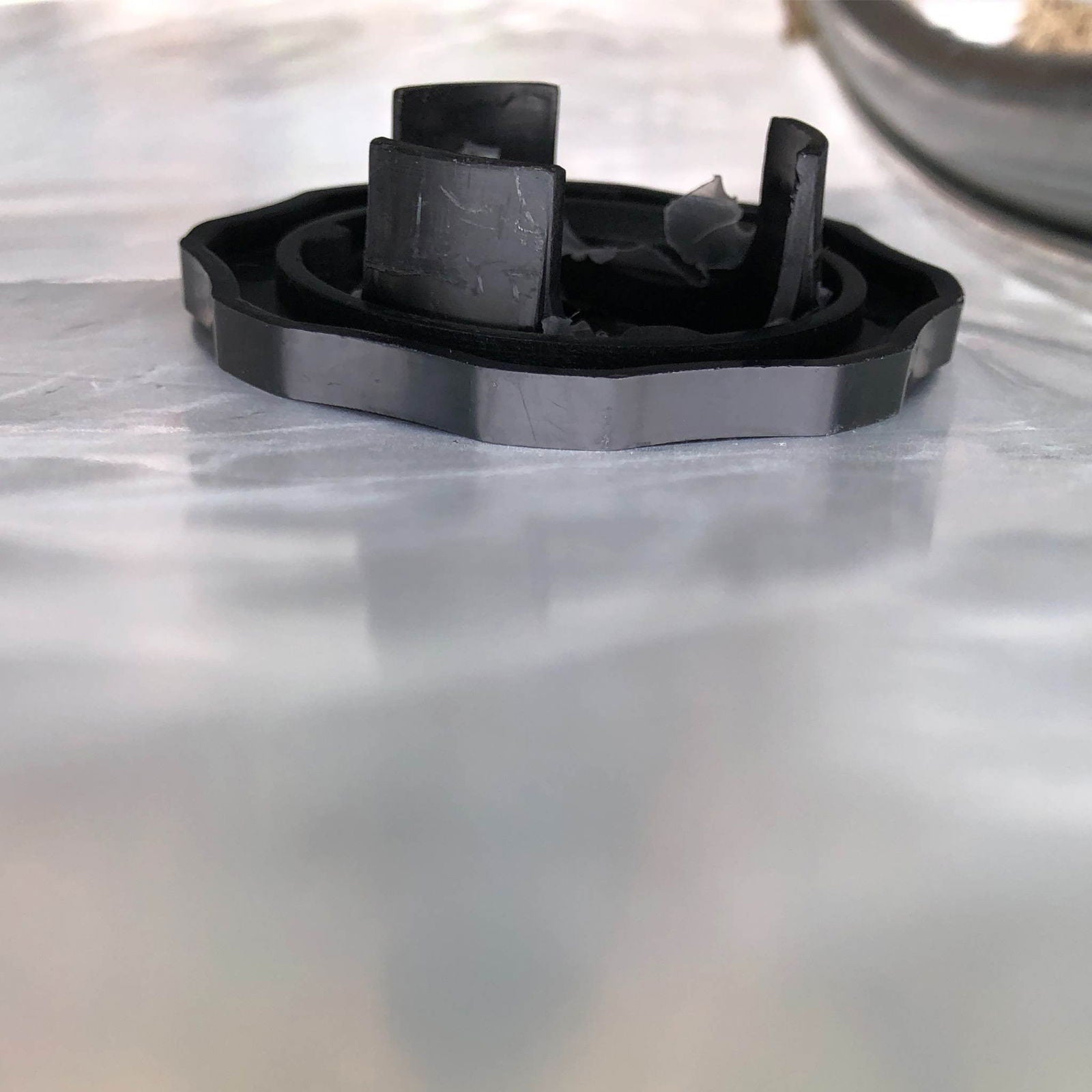 A close-up of the Bootstrap Farmer Air Inflation Jumper Hose shows its black plastic base with upright sections on a reflective surface, resembling parts used in double-layer greenhouse film inflation. A metallic object is also visible in the top right corner.