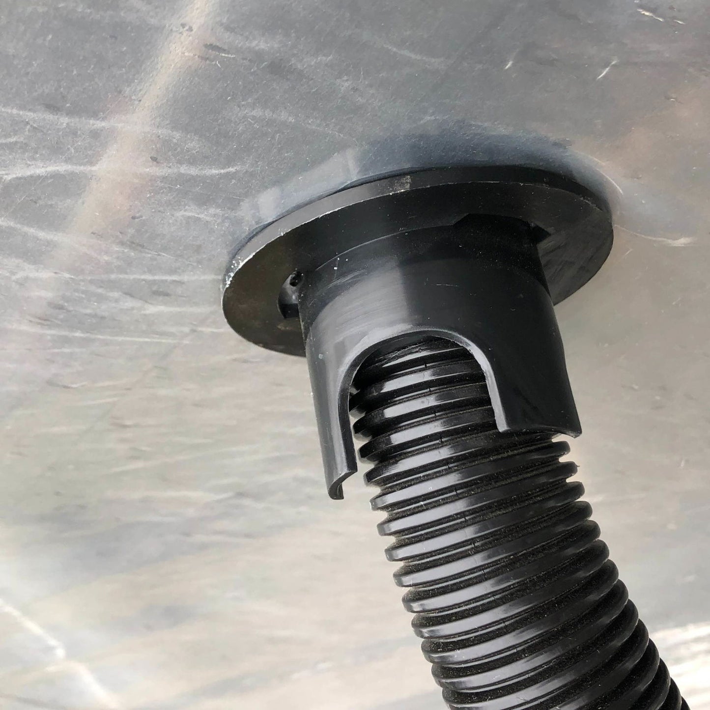 A close-up of a Bootstrap Farmer Air Inflation Jumper Hose attached to a circular fitting on a semi-transparent surface, used in double-layer film inflation systems for hoop houses.