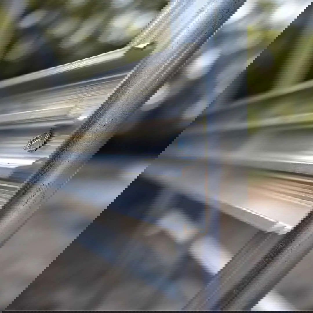 Close-up of an aluminum greenhouse component showing a silver bolt and grooved metallic texture outdoors
