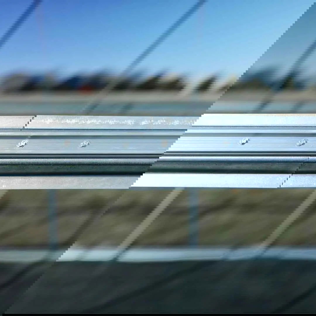 A close-up of the Bootstrap Farmer Greenhouse Steel Hip and Brace Channel shows small screws along its metallic rail, with a blurred outdoor background and diagonal, pixelated glitch lines distorting the image.