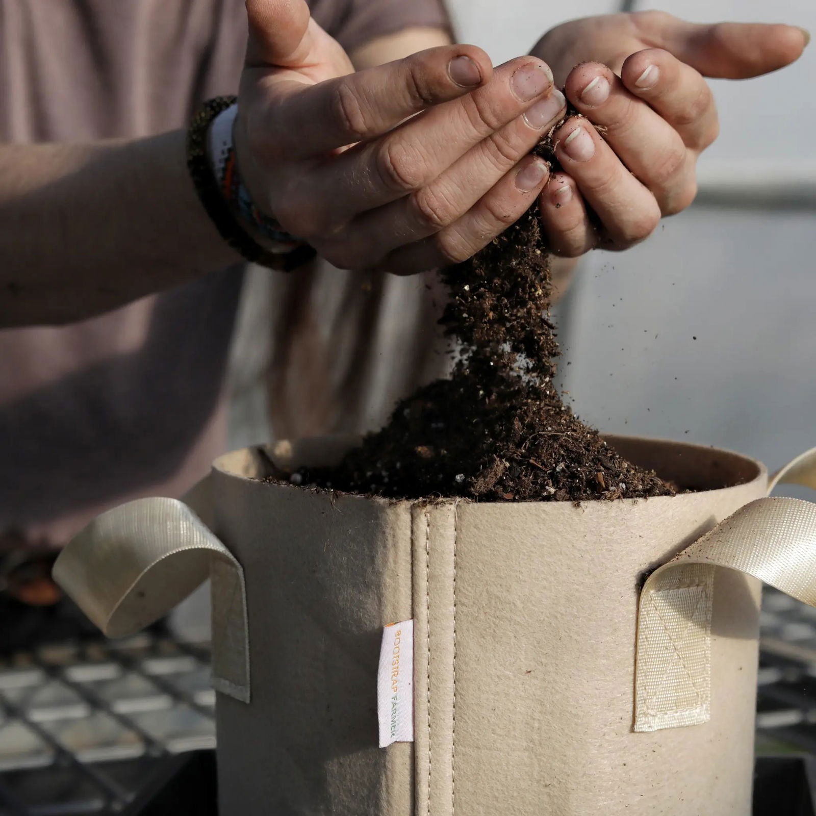 Photograph hands adding rich dark soil with visible perlite and compost to a Bootstrap Farmer grow bag outdoors
