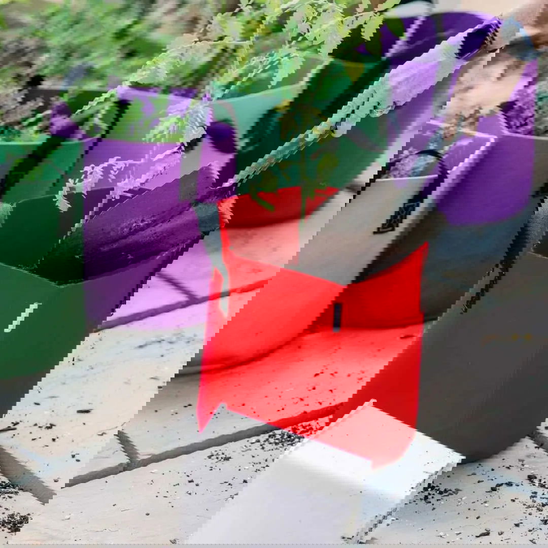 A distorted image with glitch effects shows Bootstrap Farmer’s 7 Gallon Colored Fabric Pots, featuring vibrant red, purple, and green streaks. Portable grow bags and spilled soil appear beneath the colorful watering cans.