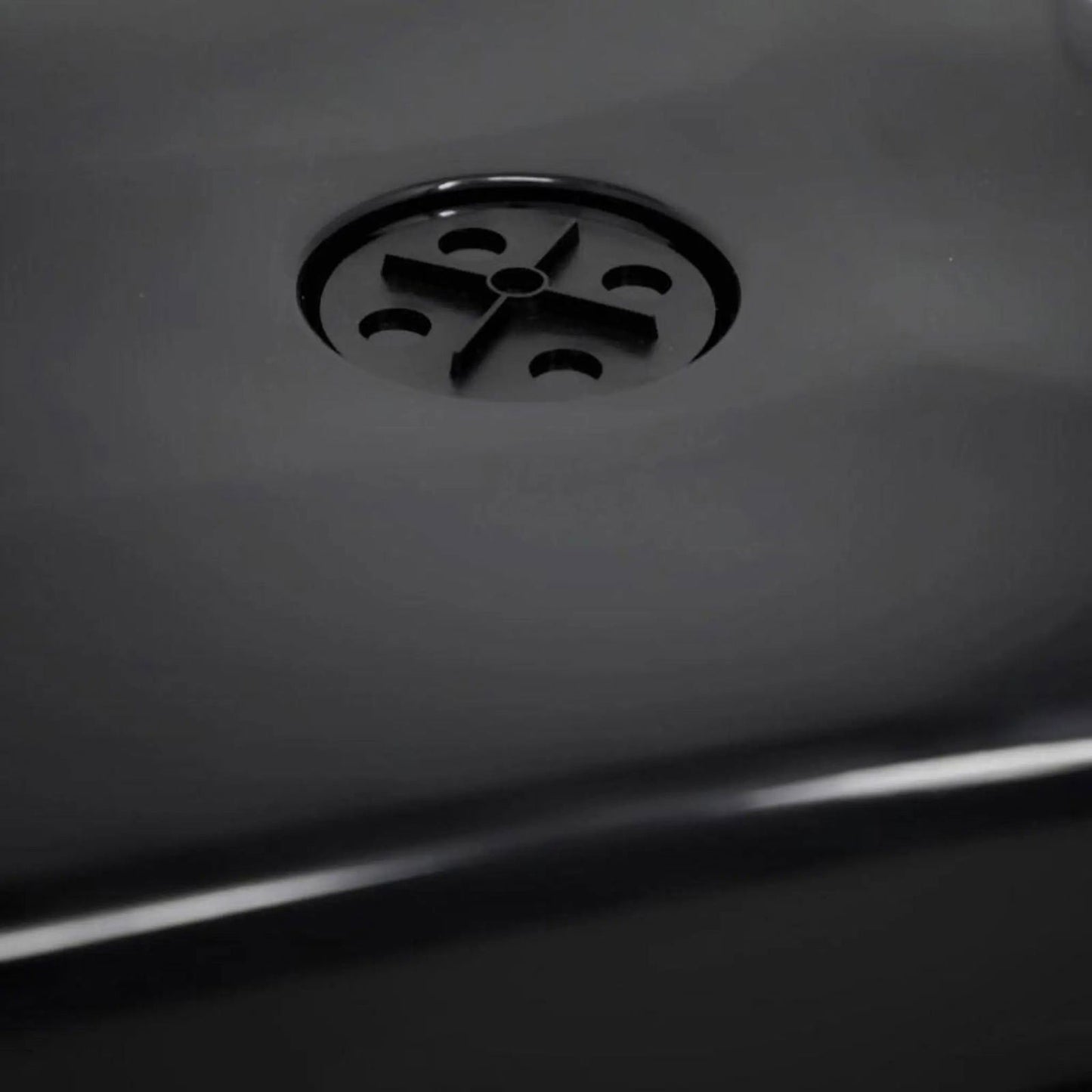 A close-up of a black surface shows a circular drain with a cross-shaped pattern, similar to those in the Bootstrap Farmer 1020 Blackout Humidity Dome used for gardening.