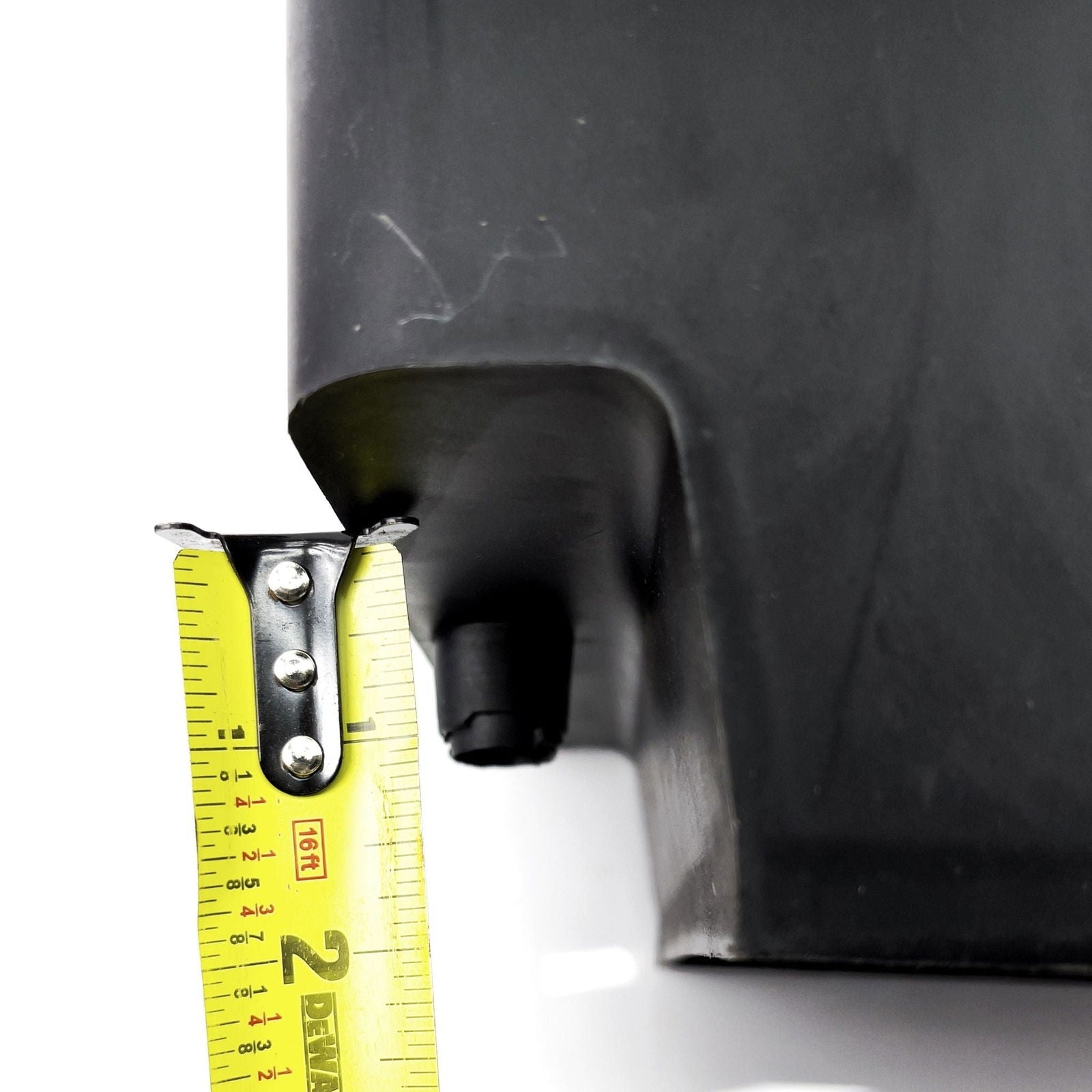 Close-up photograph showing a black plastic object being measured with a yellow tape measure featuring rivets and inch markings
