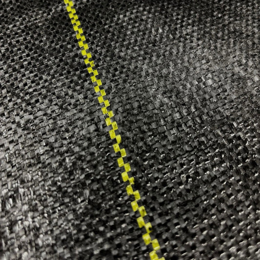 Close-up photograph of a black woven fabric with a bright yellow dashed line a textured surface and subtle light reflections

