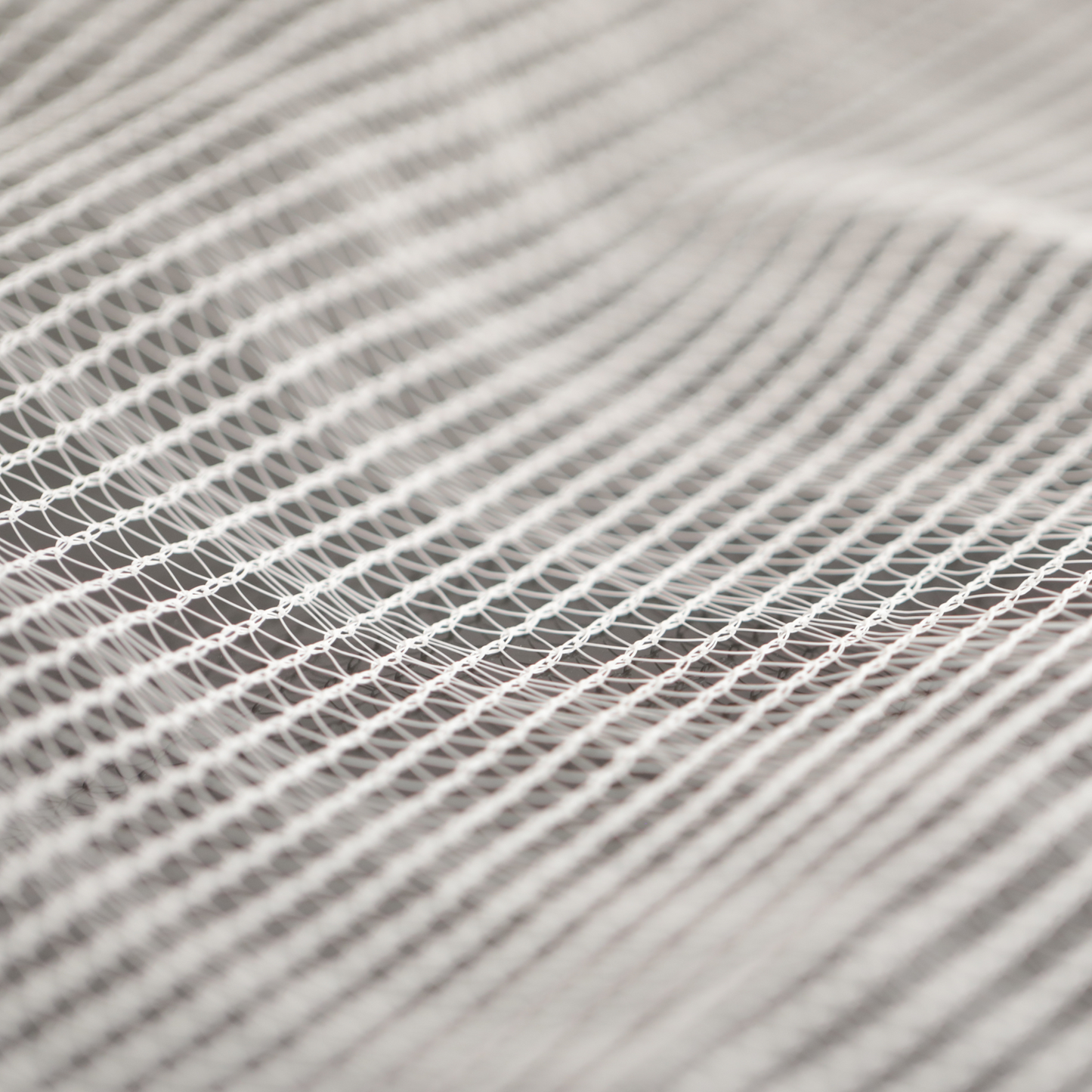 Close-up photograph of a textured white net showing its intricate knotting and subtle shadows