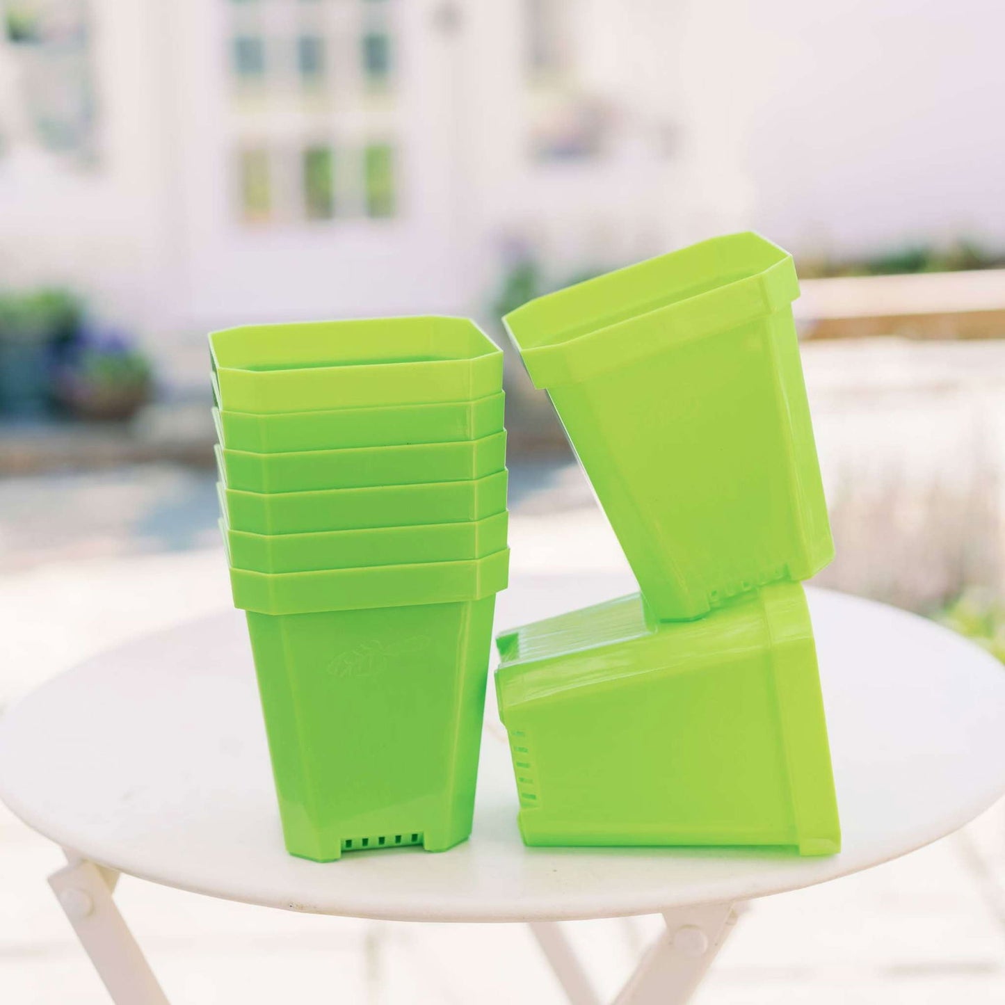 A stack of Bootstrap Farmer 5" Heavy Duty Seed Starting Pots sits on a round white table outdoors, with two pots leaning against the stack and a blurred garden or patio in the background.