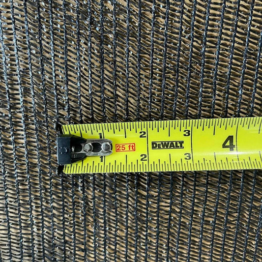 Close-up photo showing a black shade cloth texture measured with a yellow Dewalt tape measure displaying black woven pattern and  a 25ft marking
