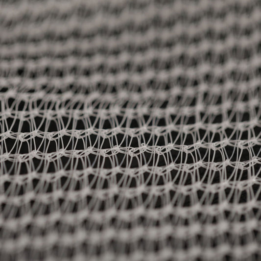 Close-up photograph of a white plastic mesh netting with a repeating pattern of knots and interweaving strands showing depth and texture
