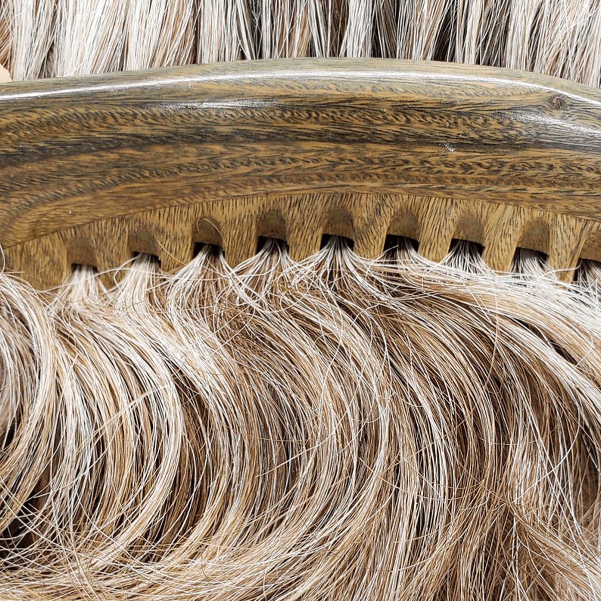 A close-up of the Sandalwood Wide Tooth Comb from ZeroWasteStore.com gliding through wavy, light brown hair with gray streaks. Its wide teeth separate and lift strands for smooth, defined waves—100% wood, plastic free, and zero waste.