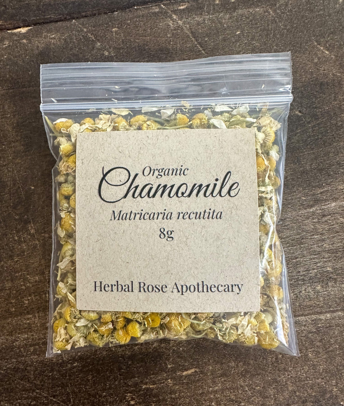 Dried organic chamomile herbs in a clear jar, showcasing small yellow and white chamomile flowers from Herbal Rose Apothecary.