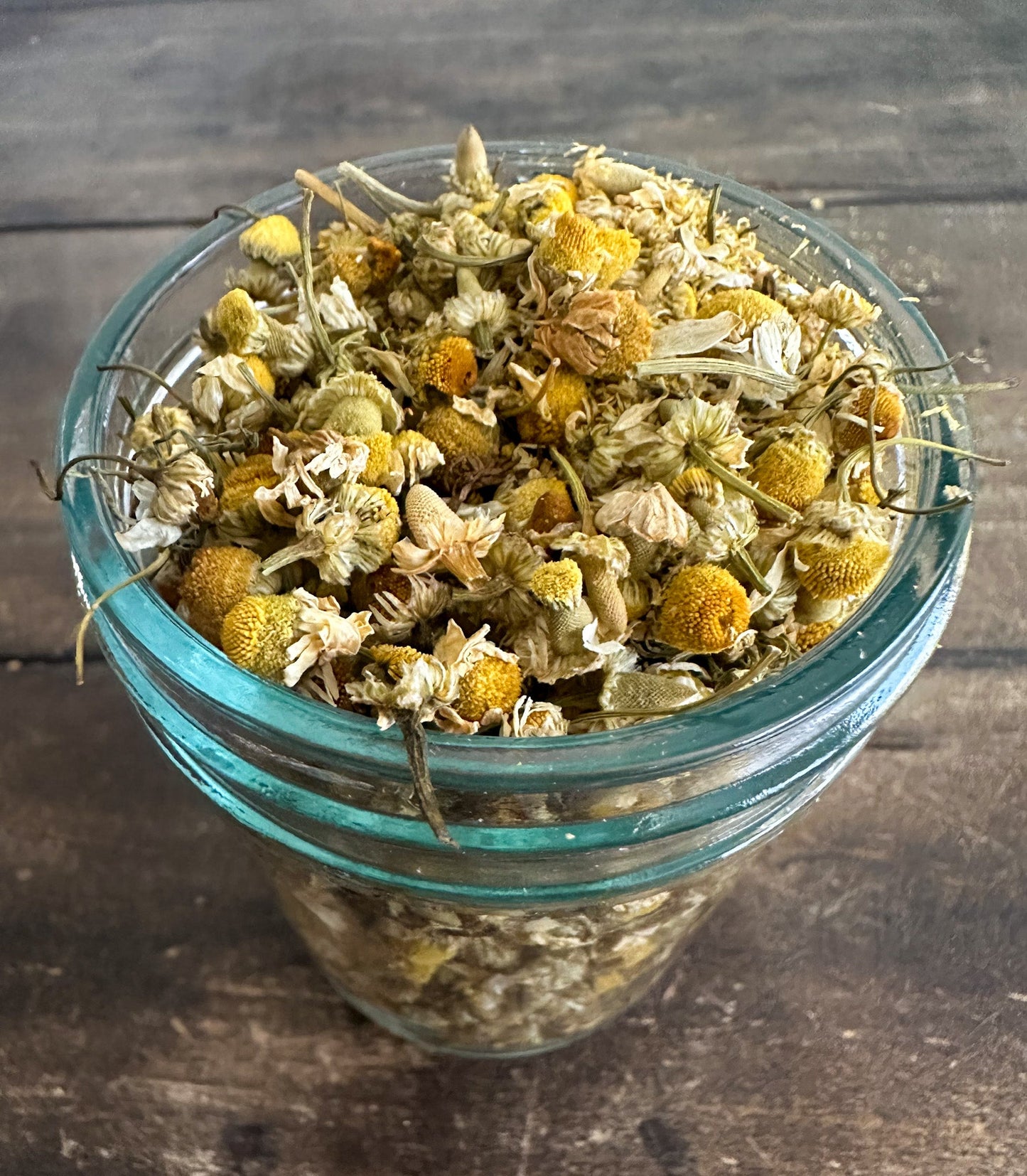 Small jar of dried chamomile herbs in an herbalroseapothecary herb jar, showcasing herbal product storage.