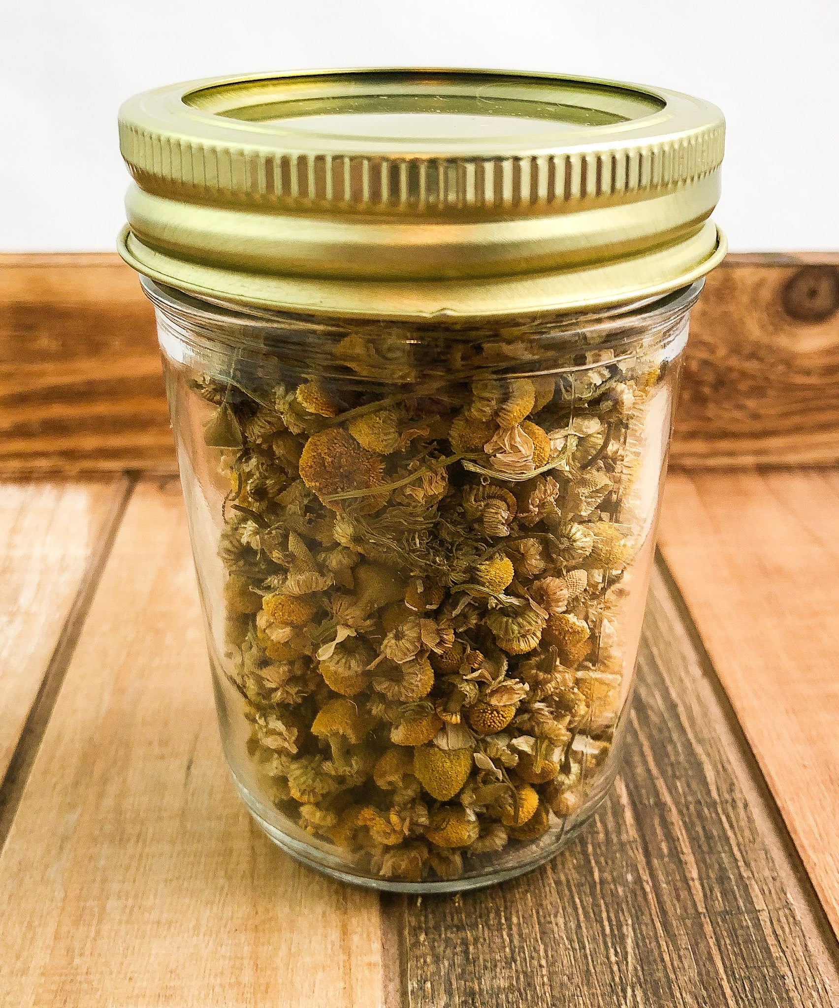 Small jar of dried chamomile herbs in a white wooden herbalroseapothecary jar for herbal tea or remedies.