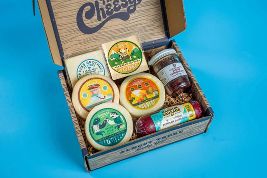 Assorted cheese and charcuterie meats in a gift box from Cheese Brothers, Inc., featuring crackers, nuts, and fresh fruit.