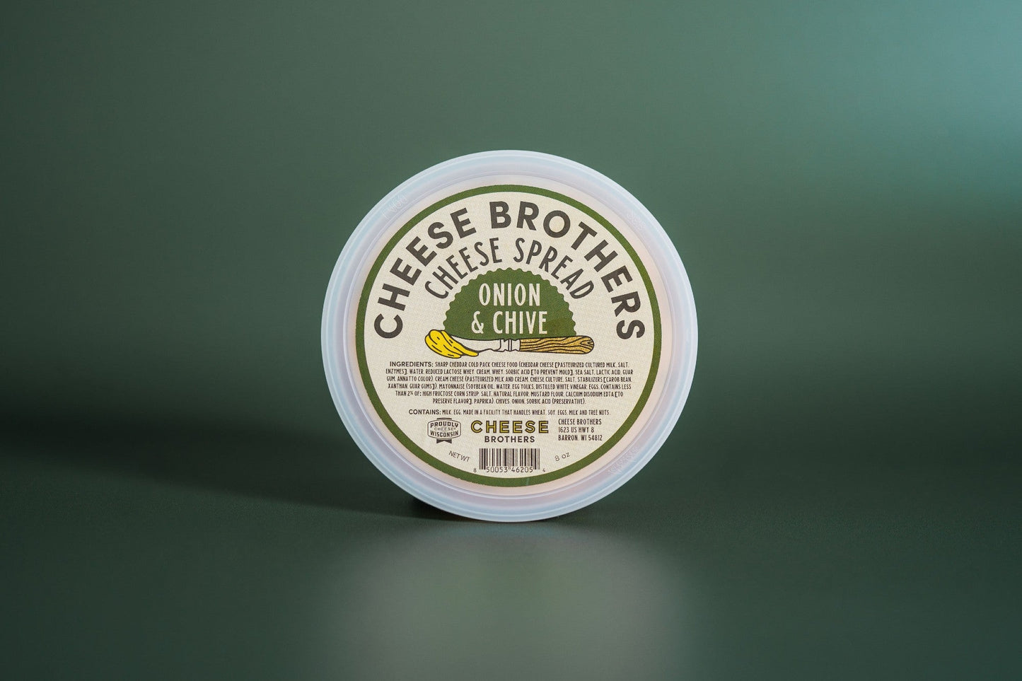 Creamy onion and chive cheese spread by Cheese Brothers, Inc. in a jar with visible herbs and smooth texture.