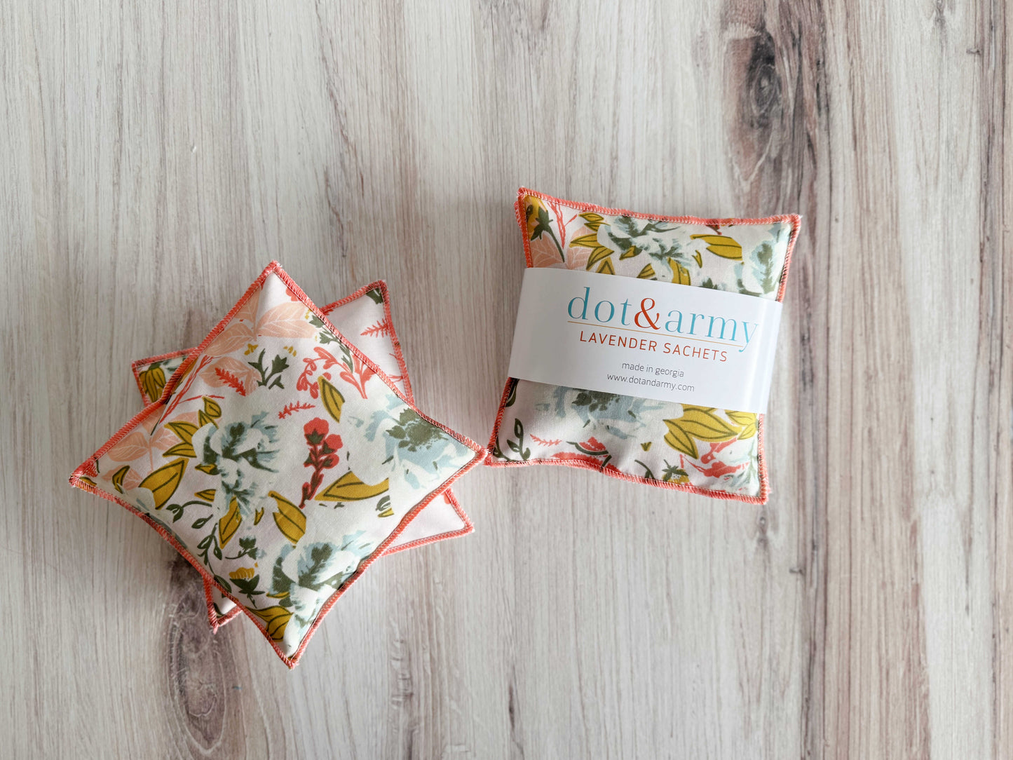 A set of two small, square lavender sachets from Dot and Army—Coral and Blue—feature floral fabric with coral trim. Filled with natural lavender, they're ideal as drawer fresheners. One sachet is labeled "dot&army LAVENDER SACHETS.