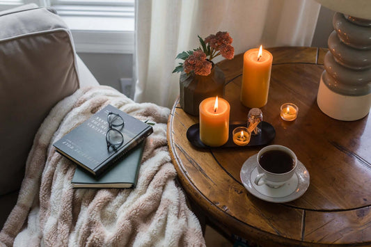 Bluecorn Candles pure beeswax pillar candles glowing in a cozy reading scene with tea, books, and glass holders.