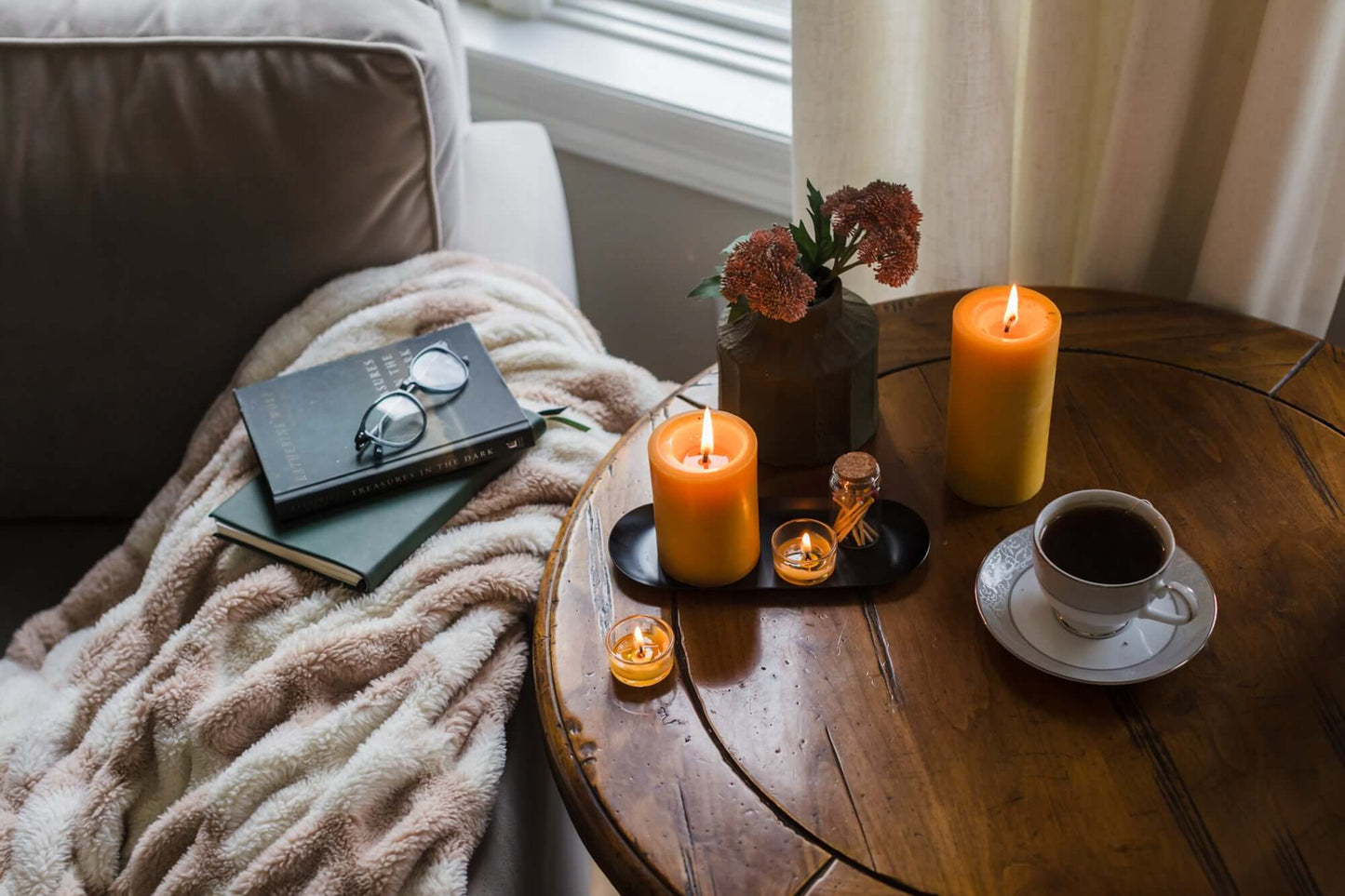 Bluecorn Candles pure beeswax tea light candles glowing in glass holders, surrounded by books, tea, and a cozy reading scene.
