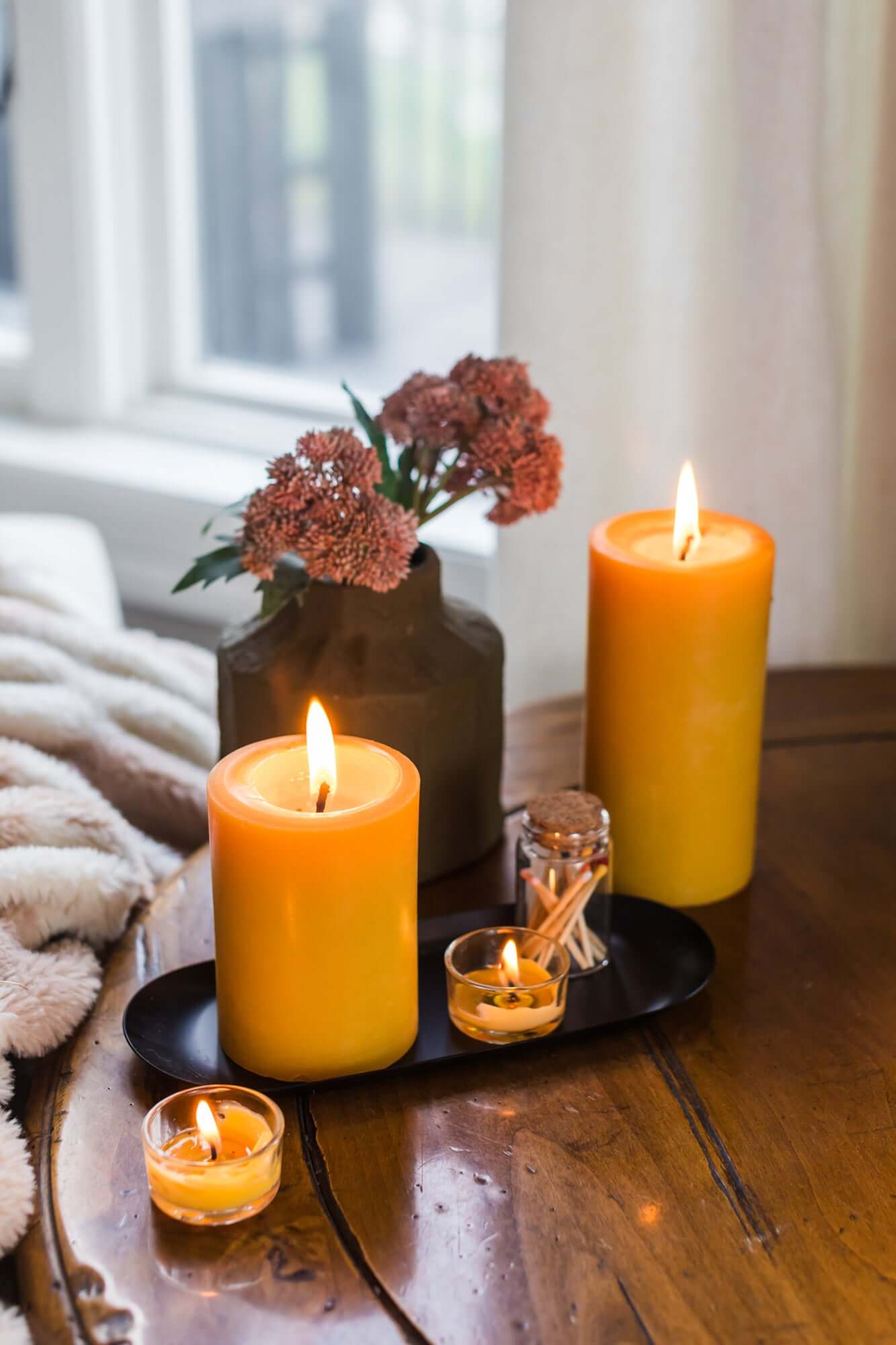 Bluecorn Candles pure beeswax pillar candles glowing in a cozy reading scene with tea, books, and a comfy chair.