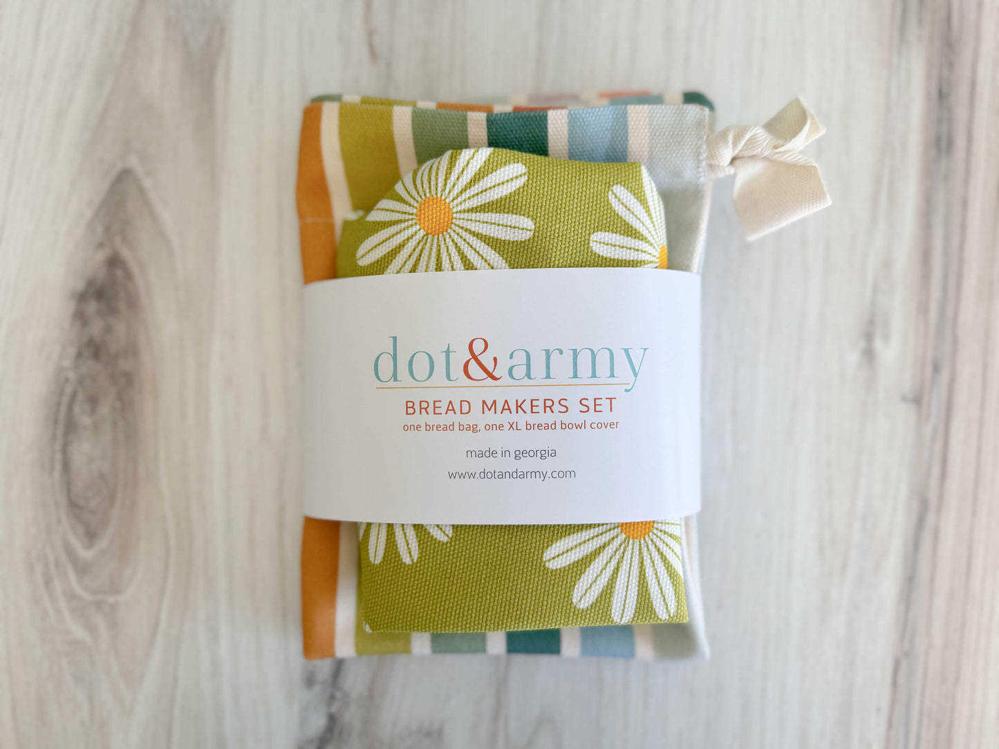Dot and Army's Daisy and Stripe Bread Makers Set includes a green linen blend bread bag with white daisies and a striped bowl cover, both wrapped in branded paper, shown on a light wood surface.