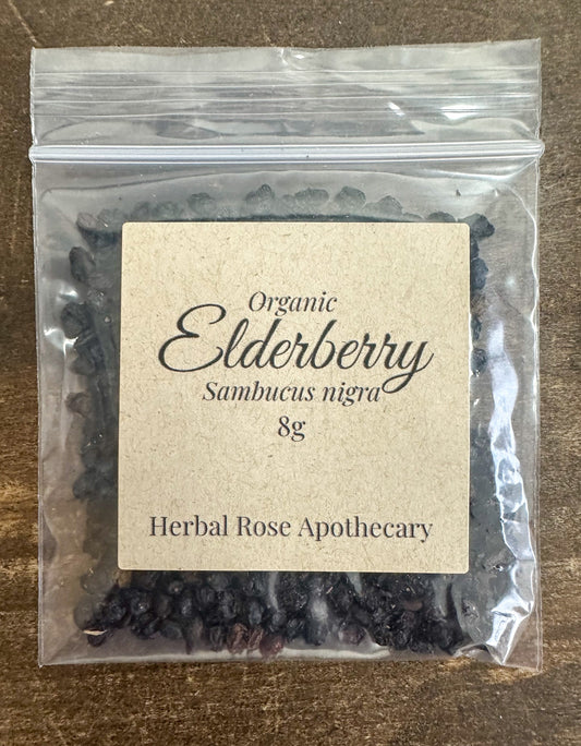 Dried organic elderberries from Herbal Rose Apothecary in an 8g package, showcasing small dark purple berries used for herbal remedies.