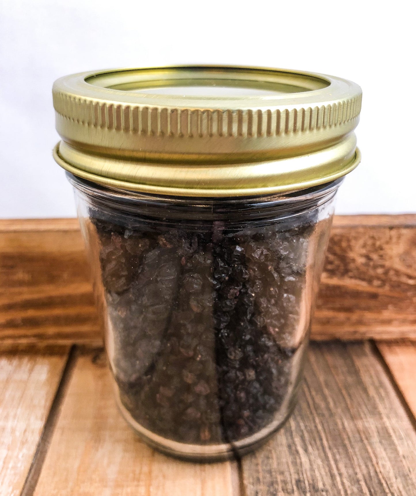 Small jar of dried elderberries in herbalroseapothecary herb jars, with a white lid and wooden accents.