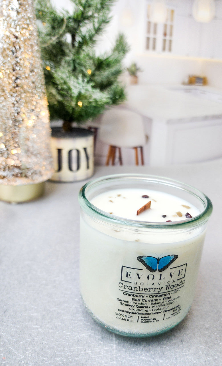 Evolve Botanica Cranberry Woods soy candle with wood wick, garnet and smoky quartz gemstones, in a decorative glass jar.