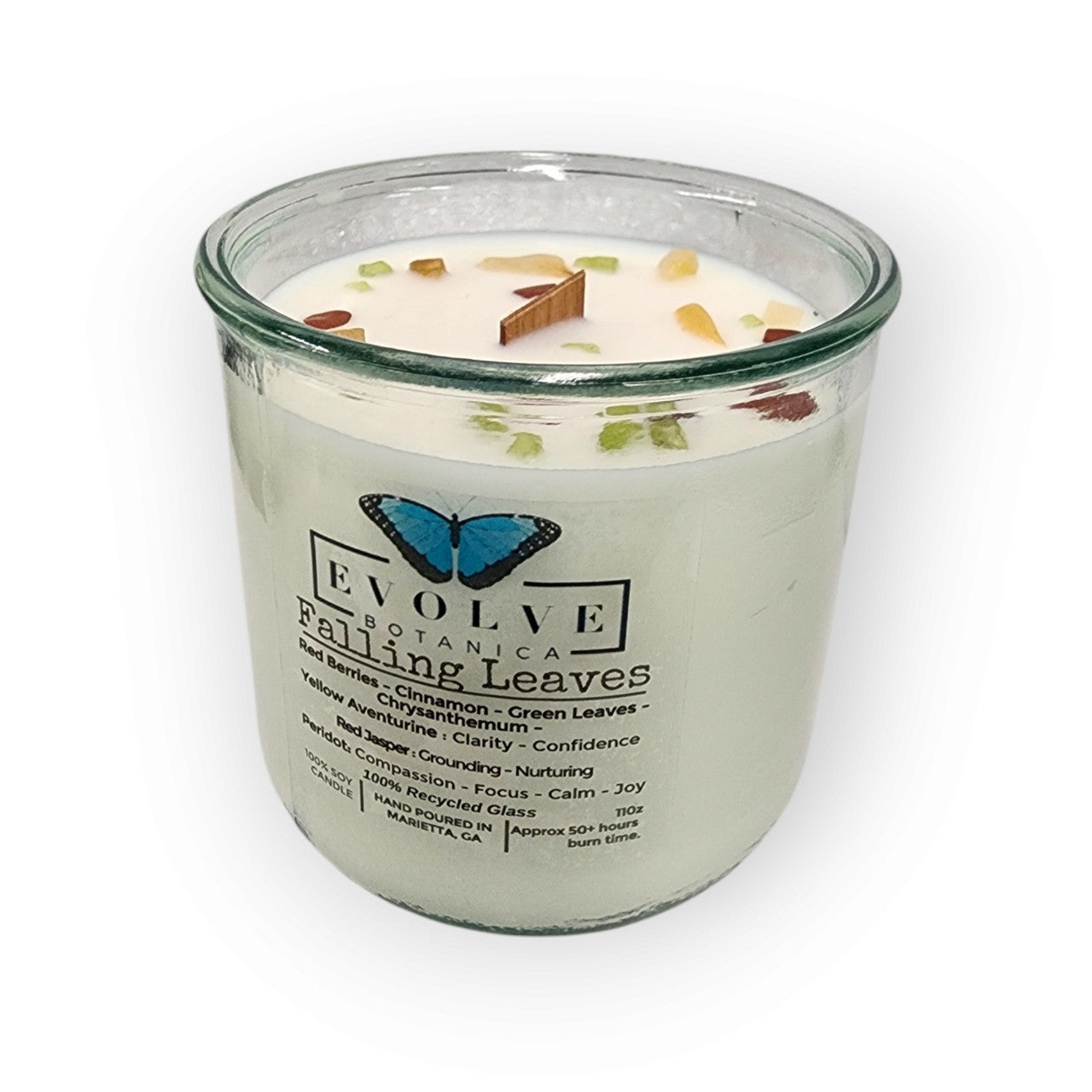 Soy candle by Evolve Botanica with a wood wick, featuring peridot, red jasper, and yellow aventurine gemstones on a decorative surface.