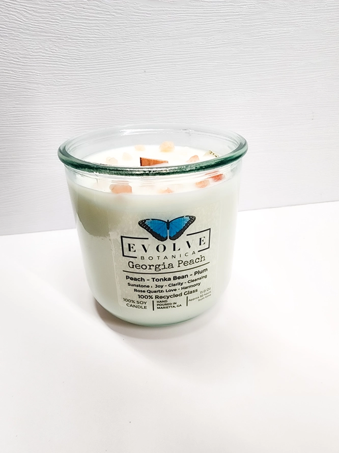 Evolve Botanica Georgia Peach Rocks Candle with wood wick, gemstone accents, soy wax, and peach scent, displayed in a decorative jar.